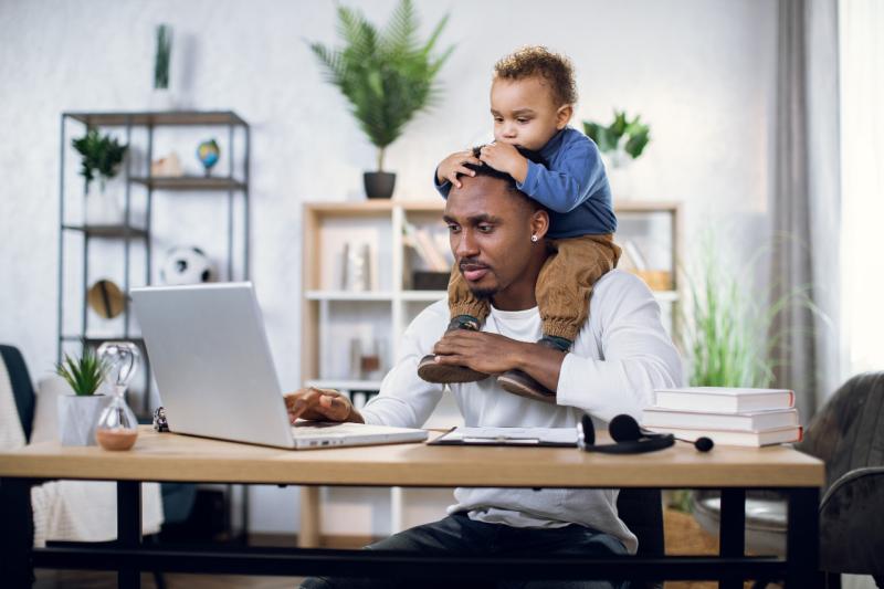 a father on the computer with his infant son on his shoulders